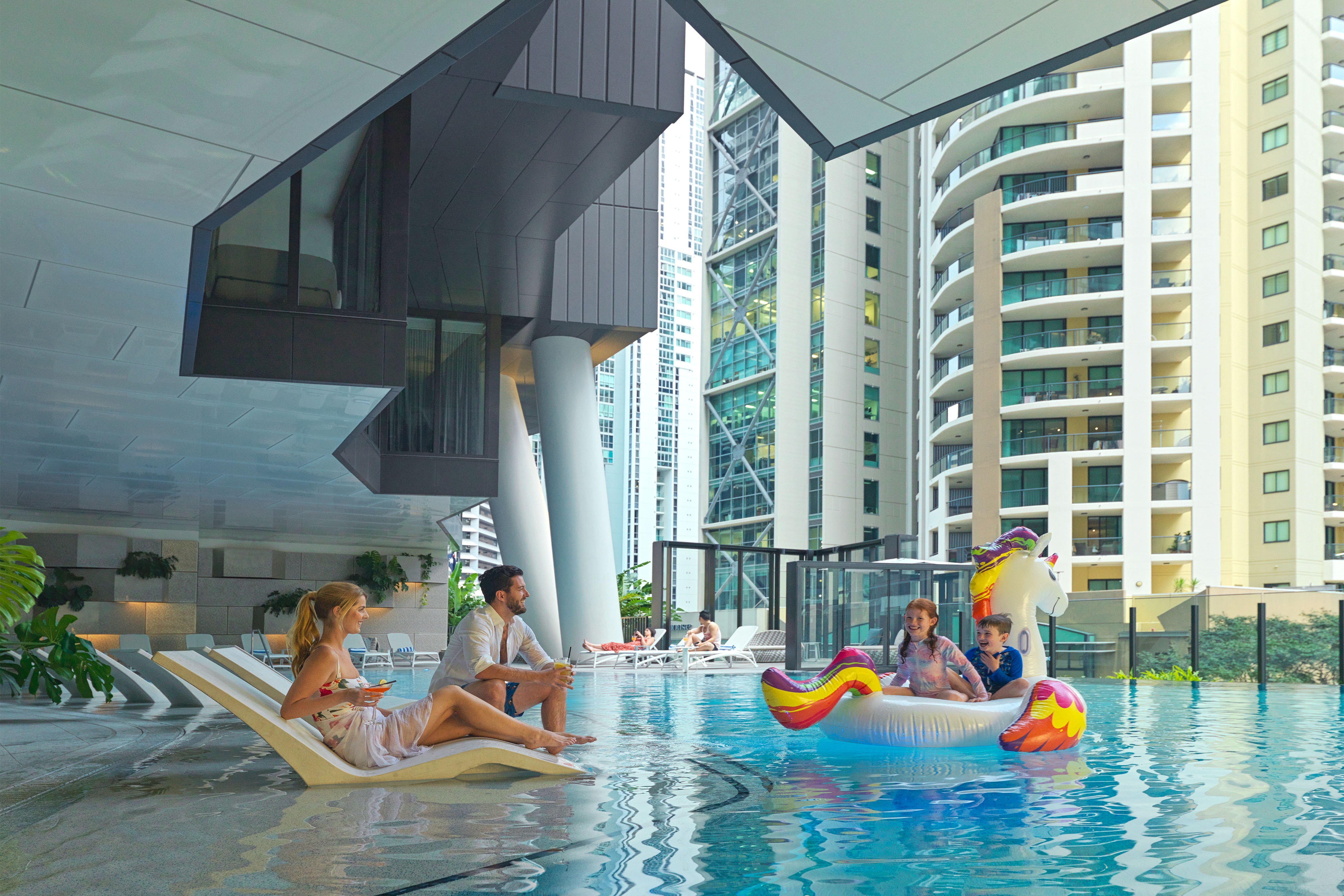 Parents watching their children play on an inflatable swimming toy shaped like a unicorn